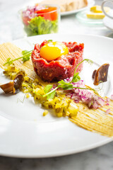Traditional beef tartar served with a raw egg on top, onion and cucumber in white plate ready to be eaten