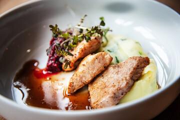 Delicious roasted pork filet cooked with smashed potatoes and smashed beetroots served in white plate.