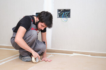 Young painter using tape and cardboard to cover the floor before painting.