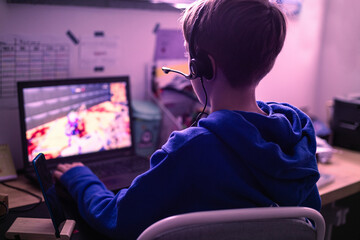 Child gaming on laptop playing addictive online video game at home in his room.