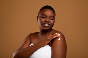 Beautiful young african american woman applying body moisturizer on shoulders