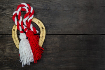 a martisor with wool tassels and a horseshoe on a rustic background