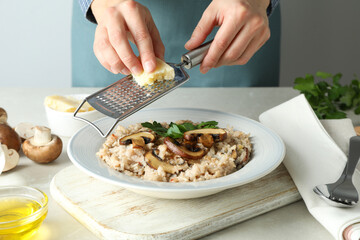 Female chef grate cheese on risotto with mushrooms