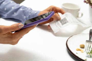 A woman scans a QR code using a phone in a cafe.