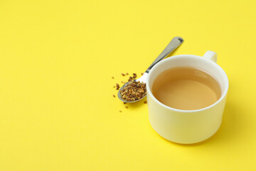 Cup and spoon with buckwheat tea on yellow background