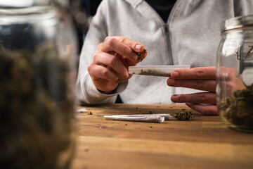 Man rolling marijuana cannabis joint in coffee shop Amsterdam with CBD weed buds in glass jars.