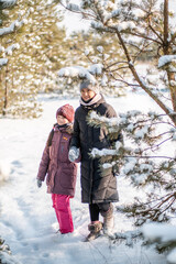 Fototapeta premium Mother and daughter are walking in the winter forest. Winter trip with family in the forest.