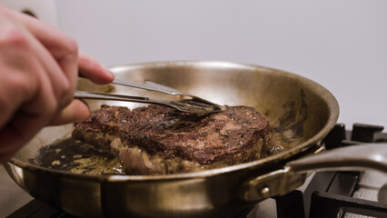 Hand turning over the steak fried in a pan with frying shovel. Golden brown, medium well-fried steak, handheld close-up shot.