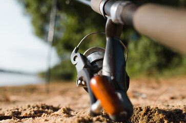 Spinning rod, steel reel on shore near water outdoors, close-up. Fishing hobby and sport concept. Selective soft focus