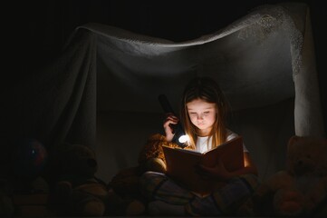 Obraz na płótnie Canvas A pretty little girl reading a book on the floor under the lamp. Children and education.