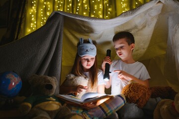 Obraz na płótnie Canvas reading and family games in children's tent. boy and girl with book and flashlight before going to bed