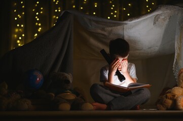 the child is reading a book with a flashlight