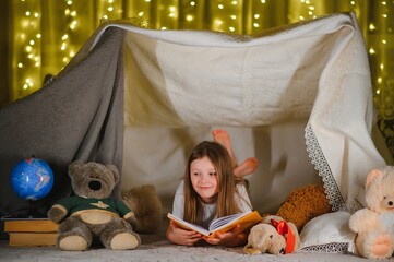 Obraz na płótnie Canvas child girl reading with book and flashlight and teddy bear in tent. before going to bed