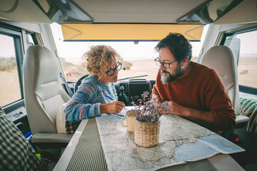 Adult couple planning next travel destination sitting inside a camper van using a paper map guide...