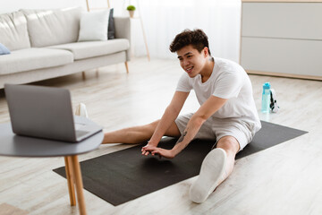 Asian guy doing stretching exercise using laptop