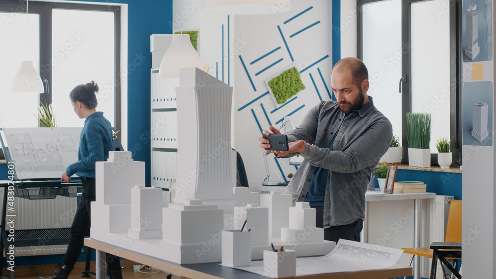 Poster man engineer using smartphone to work on building model and layout in architectural office. architec
