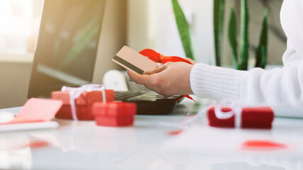 Woman holds a credit card and gift in her hands opposite the laptop. Online shopping. Valentine's Day gifts. 14 February on COVID-19 pandemic. Home delivery. Shopping online during holidays. Isolation
