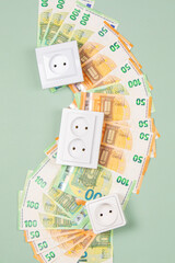 Electric sockets with Euro banknotes on light green background. Electricity cost and expensive energy concept. Top view