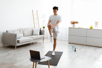 Asian guy doing standing knee to chest exercise using laptop