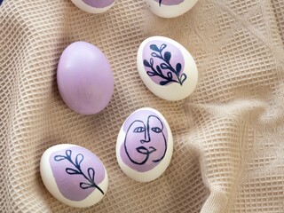 Beautiful Easter colored eggs on a kitchen towel. The eggs are painted with a floral ornament and a human face in purple. Place for text. Easter concept.