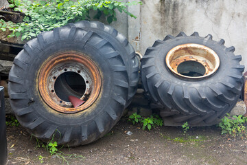 three large old used rusty truck wheels and tires next to a concrete wall close up