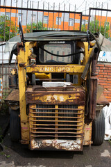 old abandoned damaged rusty yellow mini loader tractor vertical close up back view