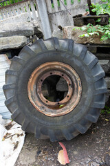 large old used rusty truck wheel and tire next to a concrete wall vertical close up