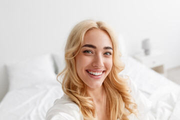 Smiling millennial european blonde lady in bathrobe enjoying good morning and makes selfie