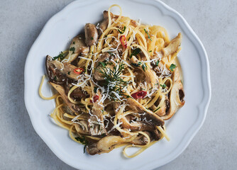 Oyster Mushroom linguini pasta closeup on white plate. Mushroom traditional pasta with parmesan cheese and red chilly peppers garnished with dill and parsley. Oyster mushroom linguini pasta - obrazy, fototapety, plakaty