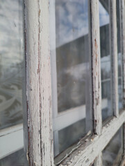Old window with peeling white paint on the frame, focus on foreground window perspective