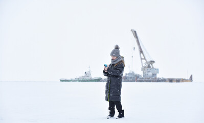a child in winter clothes on ice against the background of a sea crane