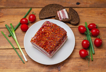 Smoked spicy bacon on a plate. Slice of smoked pork meat on bread, cherry tomatoes and green onion on wooden table.