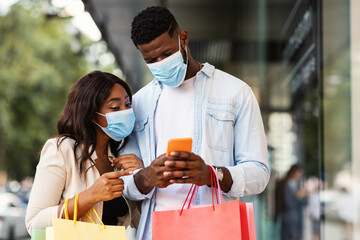 Portrait of black couple using smartphone wearing masks near mall