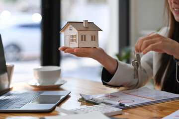 Estate agent holding house model and house key in hand. Mortgage Real estate investment and...