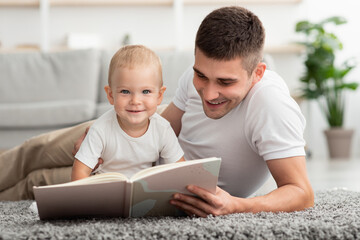 Loving Father Reading Book For His Cute Infant Baby At Home