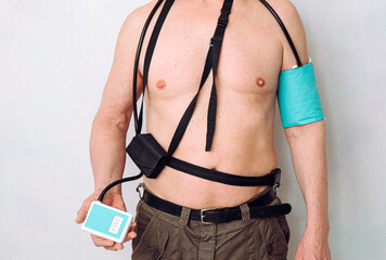 Body of a middle aged man using portable Ambulatory Blood Pressure Monitor (ABPM) for taking measurements during normal daily activities at home. - obrazy, fototapety, plakaty
