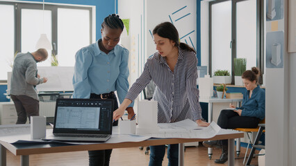 Team of workmates looking at building model and blueprints plans on table. Women architects doing teamwork to design construction layout and structure. Urban architecture project