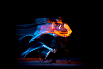 Dynamic portrait of young ballroom dancers dancing Argentine tango isolated on dark background with...