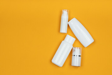 White jars and containers of cosmetics on yellow background. Skincare product set. Face and body care concept.