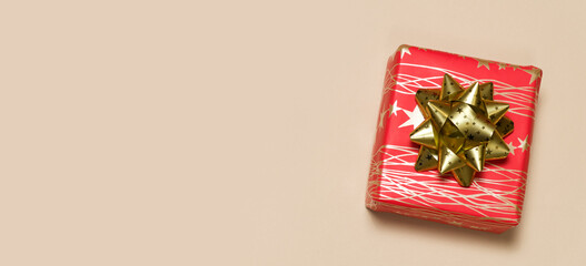 Red gift box with lines and stars with a large gold bow on a beige background, space for text