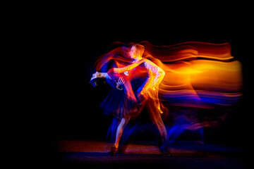 Dynamic portrait of young ballroom dancers dancing Argentine tango isolated on dark background with neon mixed light. - obrazy, fototapety, plakaty