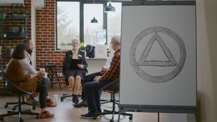 People with addiction meeting at aa group therapy session to get help from psychiatrist, having alcoholics anonymous sign on white board. Patients in circle at rehabilitation program