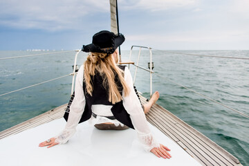 Young blond hair woman wearing in pirate costume looking ahead sitting on a yacht board sailing in...