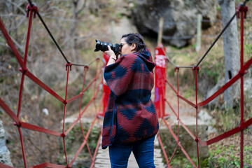Chica joven guapa tomando fotografías en entorno natural mientras pasa por rutas y puentes...
