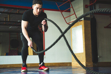 Fototapeta premium Portrait shot of strong young man during training with battle ropes in the exercise gym