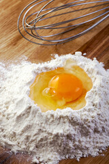 Egg in Flour and Wire Whisk on Wooden Table