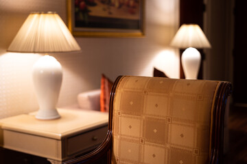 Close-up at a classic style armchair in living room with glowing lantern as background. Interior decoration and furniture object photo. Selective focus at armchair textile surface.