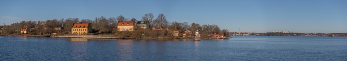 Fototapeta na wymiar Panorama view of the ness Blockhusudden, color full 1700s houses, and the skyline of the district island Lidingö a sunny winter day in the archipelago of Stockholm