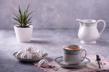 cappuccino in a classical style porcelain cup, some meringues and a small plant in the background. Still life