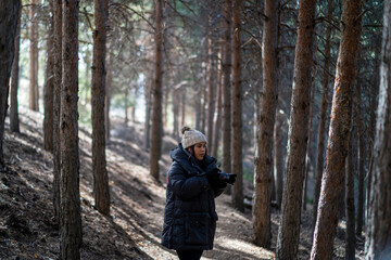 Chica joven guapa en un bosque de arboles altos con cámara de foto colgada al cuello